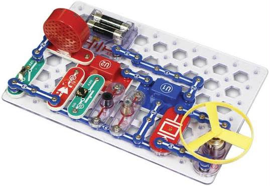 Snap Circuits Jr. kit with snap-together circuit pieces, a speaker, and a yellow fan on a clear base grid